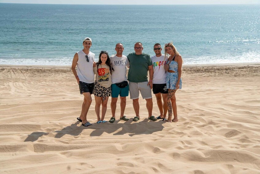 A group of people standing on a sandy beach with the ocean in the background. 3