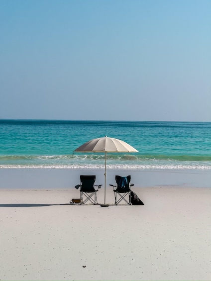 Two beach chairs and an umbrella on a sandy beach with turquoise water. 1