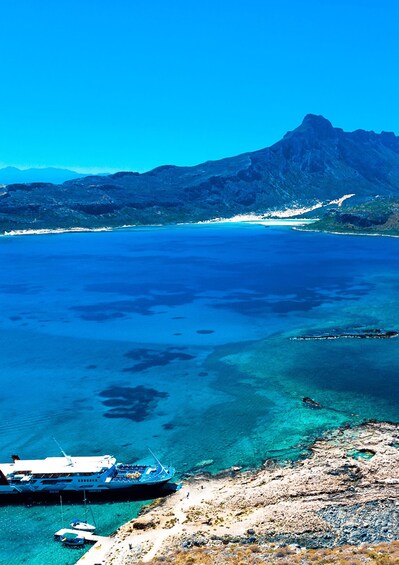 A coastal landscape with clear blue waters, a rocky shore, and a mountain in the background. 3