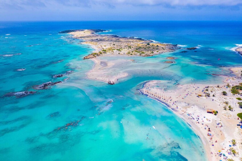 An aerial view of a coastal area with clear turquoise waters, a sandy beach, and rocky outcrops. 1