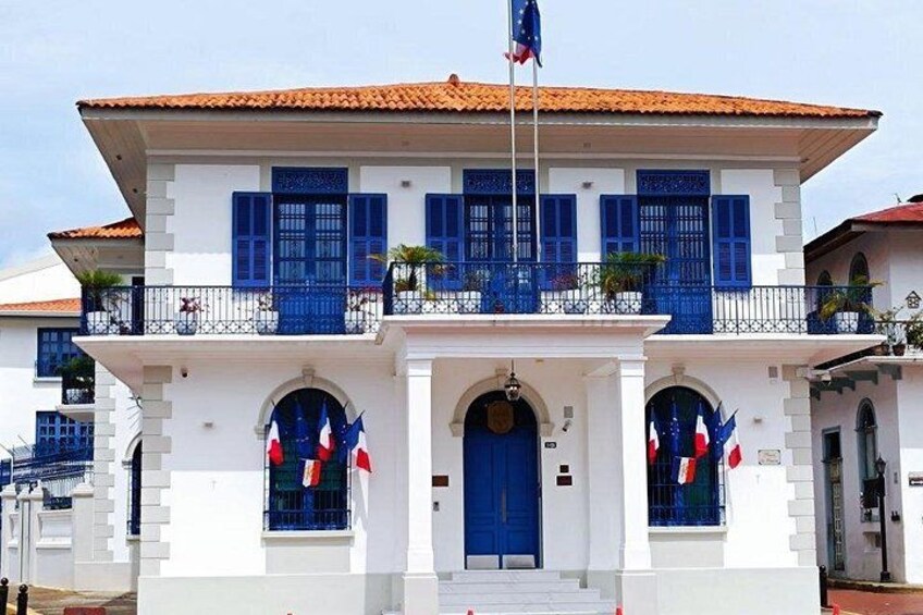 A white building with blue shutters, a red roof, and a flagpole with a flag. 2