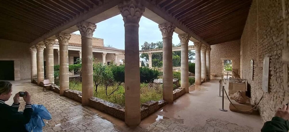 An ancient courtyard with columns, a fountain, and a view of the surrounding landscape. 3