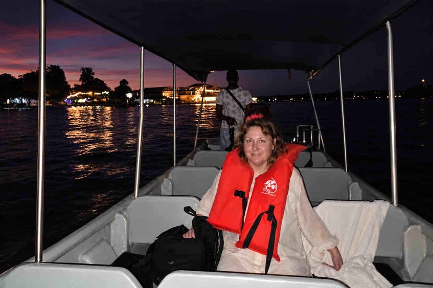 A person on a boat wearing a red life jacket, with a cityscape and water in the background. 2
