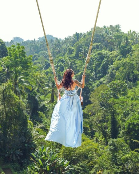 Una mujer con vestido azul se balancea en una cuerda sobre un bosque verde y frondoso. 3