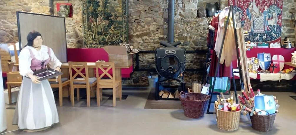 A doll in a historical setting with a stone wall, wooden furniture, a wood stove, and medieval flags. 2