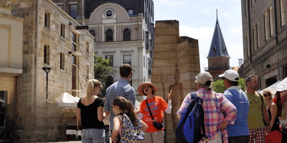 A group of people walking along a historic street with old buildings and a church spire. 4