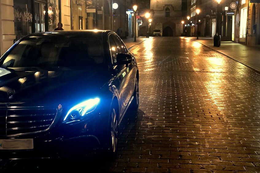 A black car parked on a wet cobblestone street at night. 2