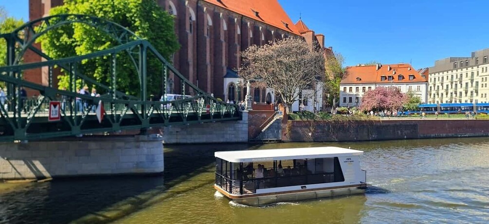 A river with a white boat, a green bridge, and buildings with red roofs. 3