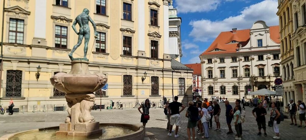 A public square with a classical fountain, historic buildings, and a clear sky. 2