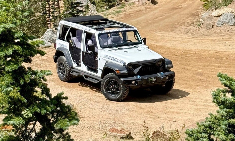 A white off-road vehicle with black accents driving on a dirt road surrounded by greenery. 2