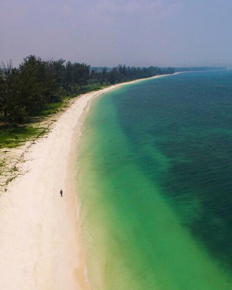 A sandy beach with clear turquoise water and a person walking along the shore. 4