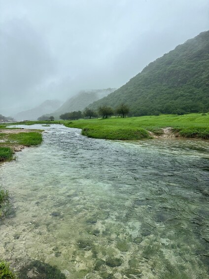 A clear river flowing through a green valley with hills in the background. 5