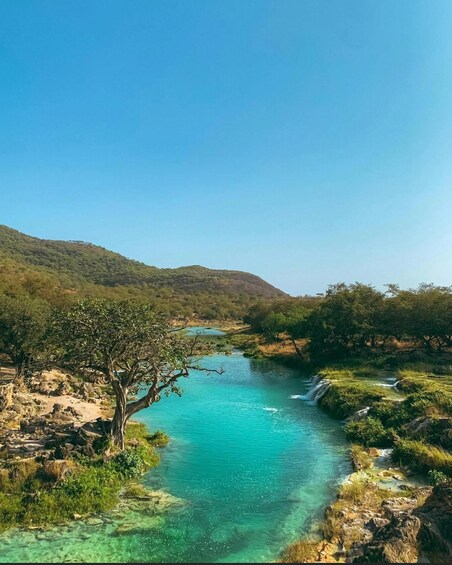 A clear river surrounded by green hills and trees. 4