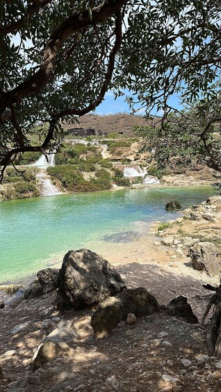 A clear turquoise pool surrounded by rocky terrain and sparse vegetation. 2