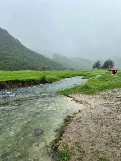 A river flowing through a green valley with a red tent on the right. 3