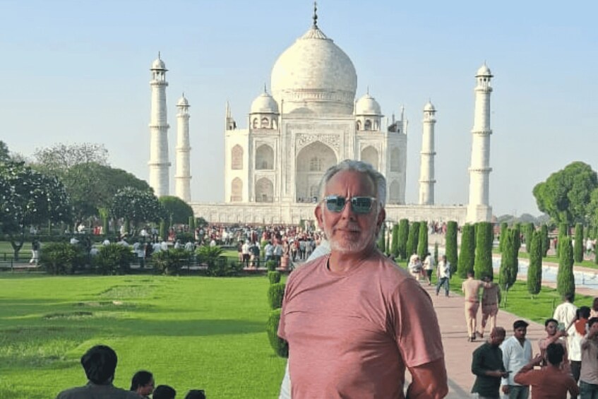 A person standing in front of the Taj Mahal with its four minarets and central dome, surrounded by a well-maintained garden and a crowd of visitors. 5