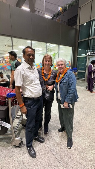Three people standing in an airport terminal with luggage carts and a 'Lost Property' sign in the background. 2