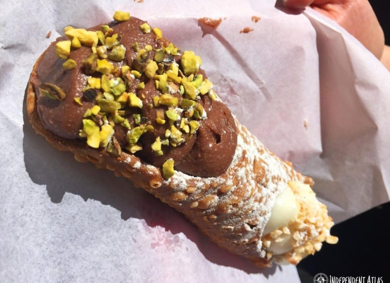 A pastry with a chocolate filling and chopped pistachios on a piece of parchment paper. 5