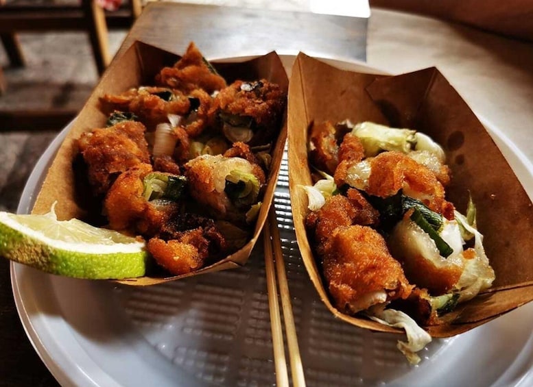 Two paper containers with fried food, including vegetables and possibly meat, on a plate. 2