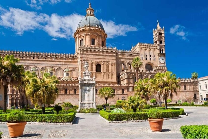 A historic building with a dome and clock tower, surrounded by well-manicured gardens and palm trees. 3