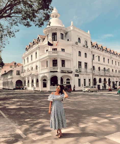 A woman in a floral dress standing in front of a large white building with a dome and balconies. 1