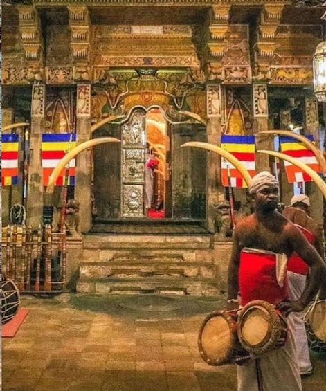 A temple entrance with ornate carvings, a central deity figure, and two individuals holding drums. 3