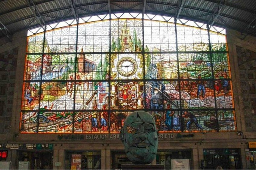 A large stained glass window with a clock, depicting a historical scene. 3