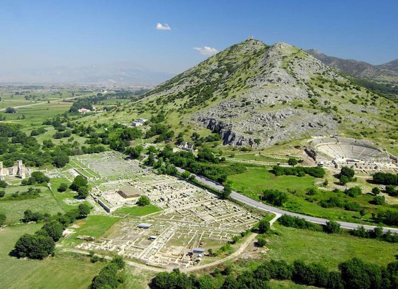 An archaeological site with ruins and a large amphitheater on a hillside. 2