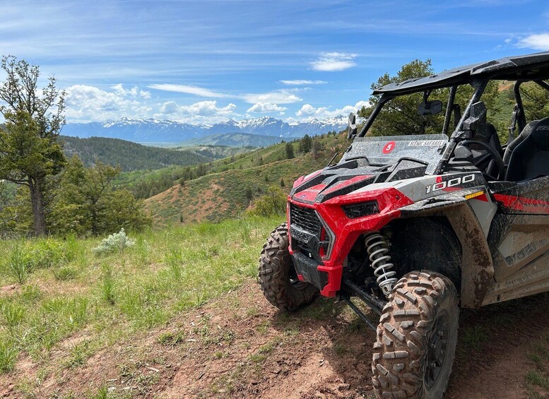 A red and white off-road vehicle on a dirt path with a mountainous landscape in the background. 1