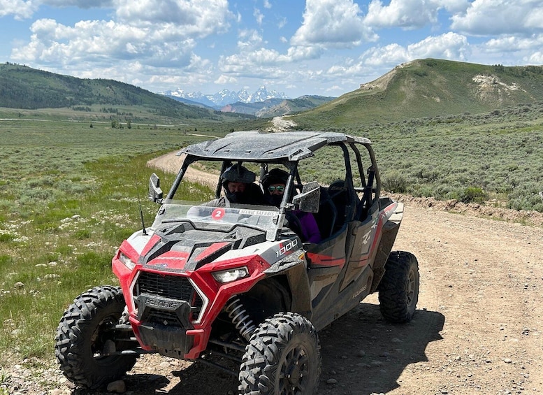 A red Polaris 1000 off-road vehicle on a dirt path with mountains in the background. 5