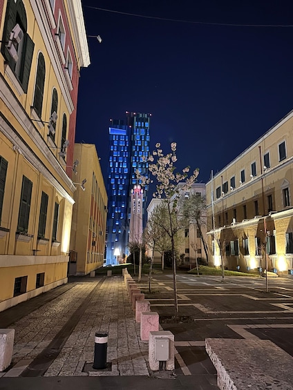 A nighttime city street with historic buildings, a modern illuminated skyscraper, and a row of trees. 5