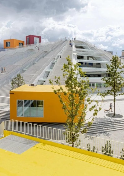 A modern architectural structure with a staircase leading to a rooftop area, surrounded by trees and a yellow building. 3