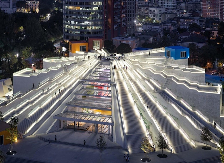 A modern architectural complex with multiple levels of stairs and glass walkways, surrounded by urban buildings. 1