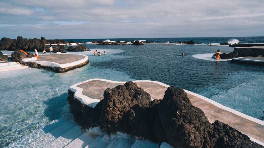 A natural hot spring with clear water, surrounded by rocks and a view of the ocean. 2