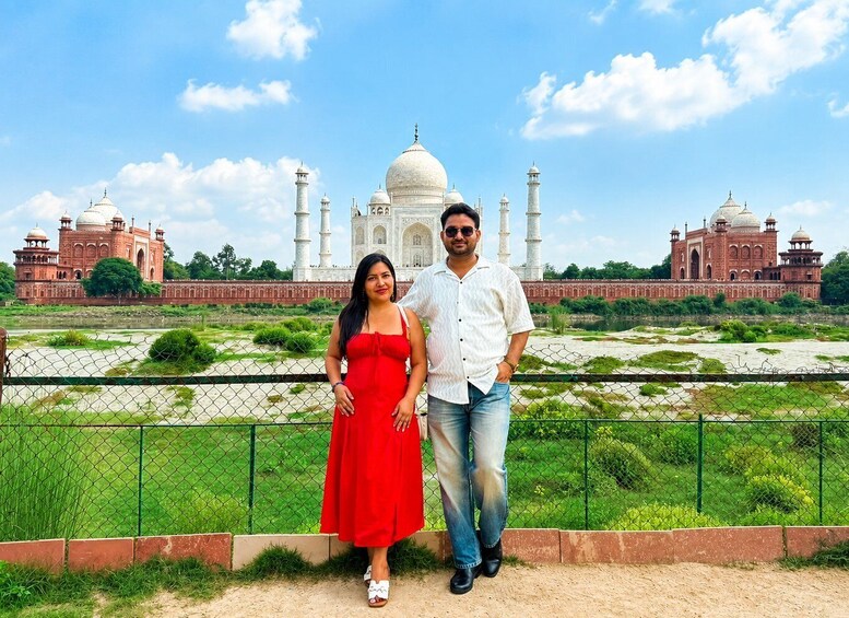 Two people standing in front of the Taj Mahal with a fence and greenery in the foreground. 3