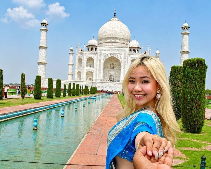 A person in a blue outfit standing in front of the Taj Mahal with a clear sky. 4