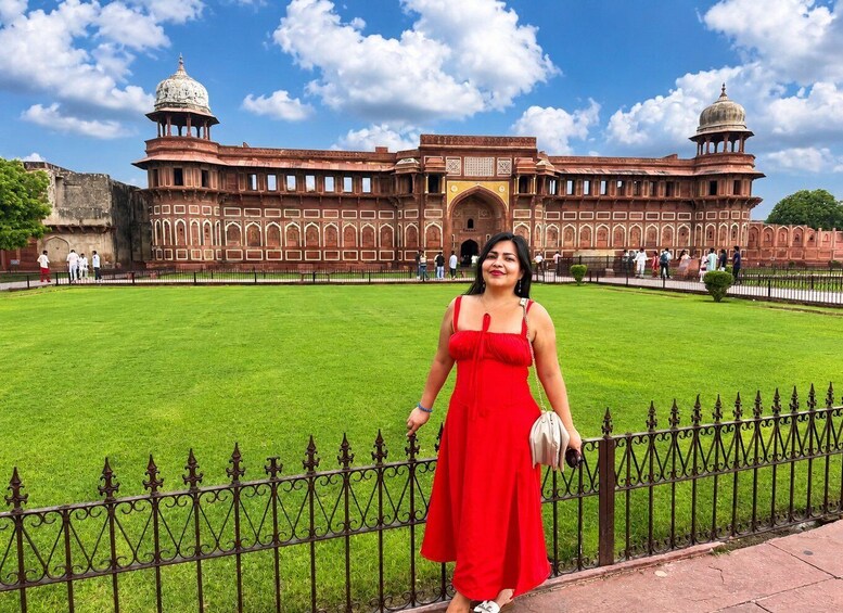 A woman in a red dress standing in front of a large, historic building with domed towers and intricate architecture. 2