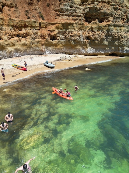 A beach with clear water, rocky cliffs, and people kayaking and swimming. 4