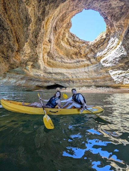 Two people kayaking in a yellow kayak with a rocky cave in the background. 2
