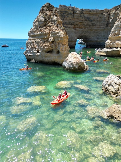 Kayakers on a clear turquoise sea with rocky formations. 1