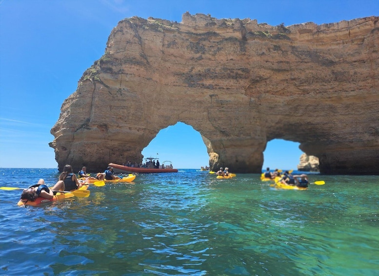 People kayaking and a boat near a large rock arch in the sea. 5