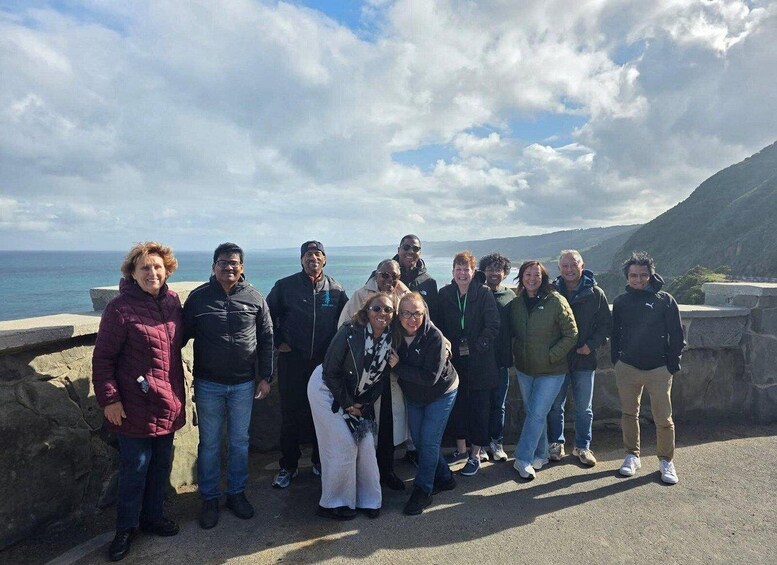 A group of people standing on a coastal road with a view of the sea and mountains in the background. 4