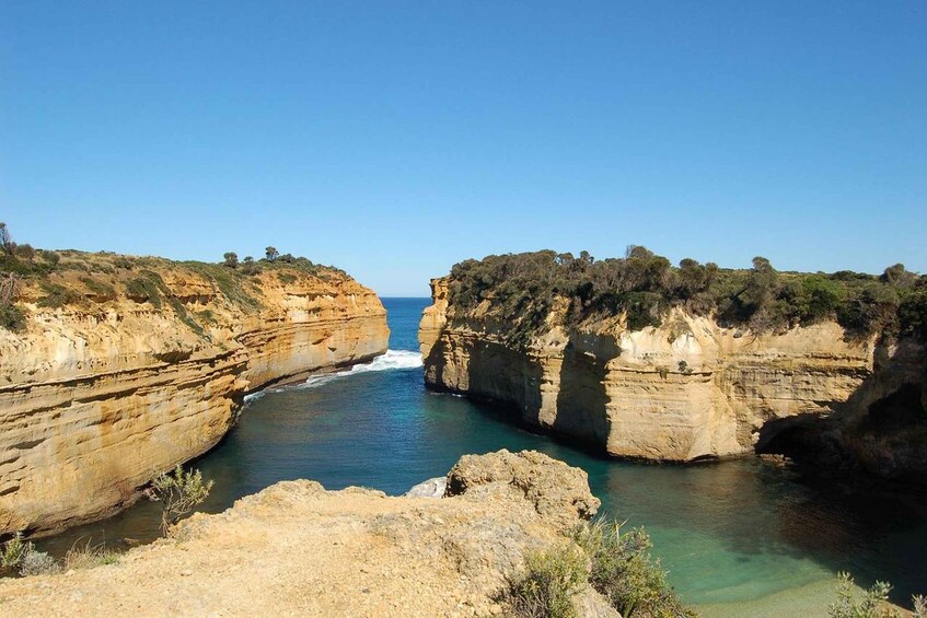 A coastal canyon with layered rock formations and a clear blue sea. 5