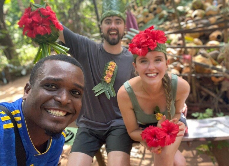 Three people outdoors with red flowers, one wearing a green headband and another with a flower in their hair. 1