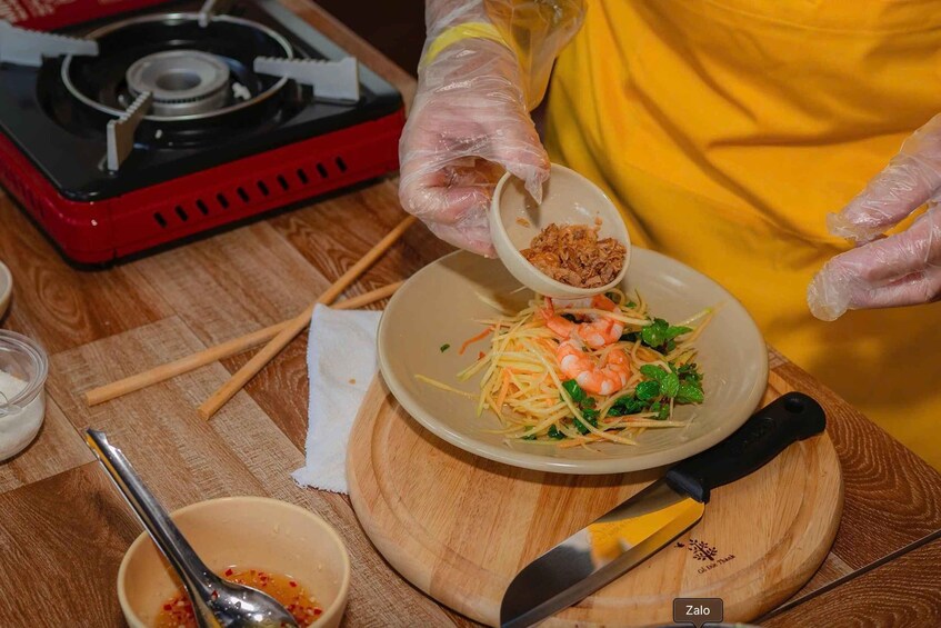 A person preparing a dish with shrimp, noodles, and greens, with a bowl of sauce and a cutting board nearby. 3