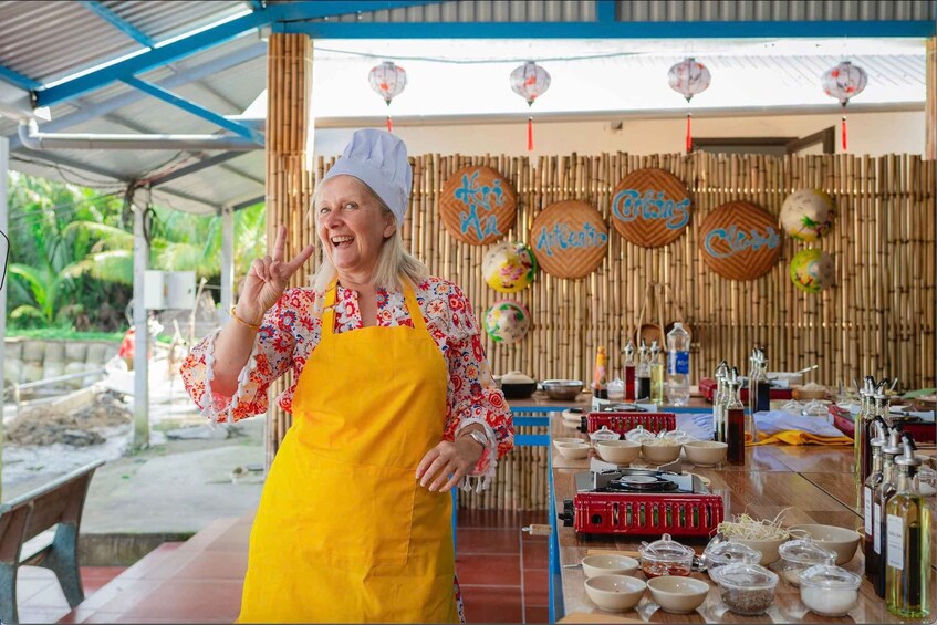 A person in a chef's outfit standing in front of a bamboo wall with decorative signs and a table with cooking utensils and ingredients. 4
