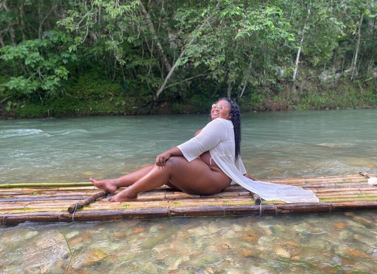 A person sitting on a bamboo raft in a river surrounded by dense greenery. 5
