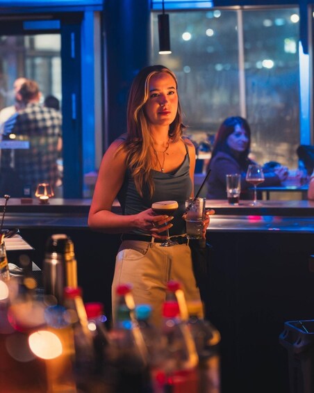 A person holding a cocktail glass at a bar with bottles and glasses on the counter. 5