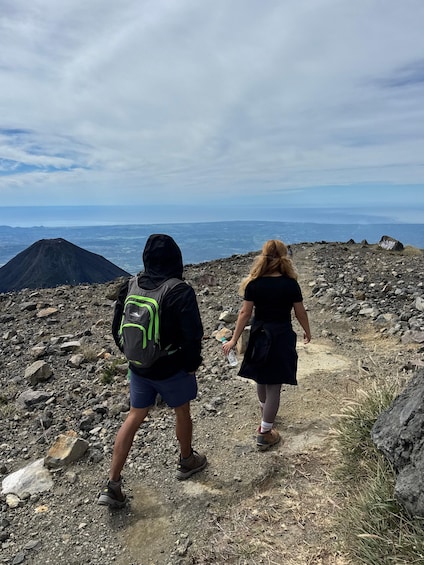Two people hiking on a rocky trail with a mountain and ocean in the background. 2