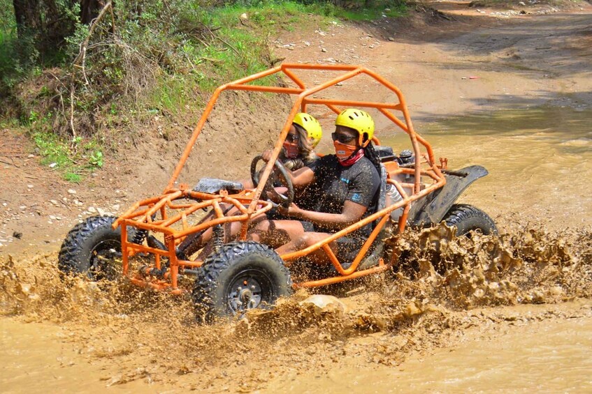 Two people in an orange off-road vehicle driving through a muddy area. 4